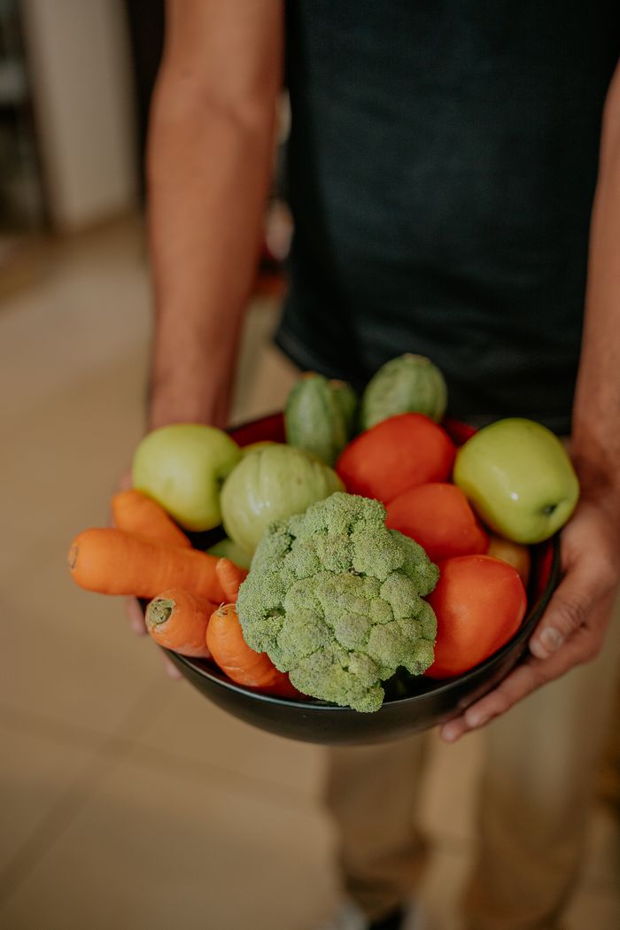 A person holding a bowl filled with fresh vegetables and fruits indoors.