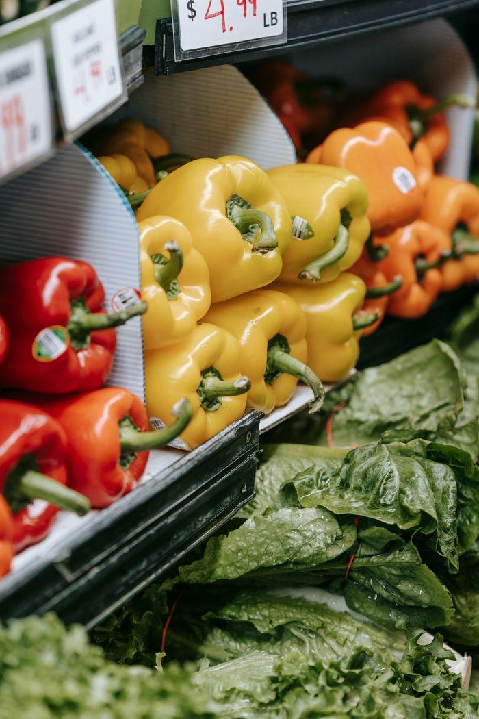 Fridge stall with ripe healthy red yellow and orange bell peppers and green spinach arranged in row in modern grocery market