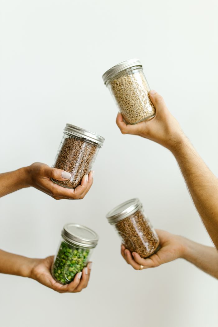 Four hands holding glass jars of grains and legumes, emphasizing kitchen organization.